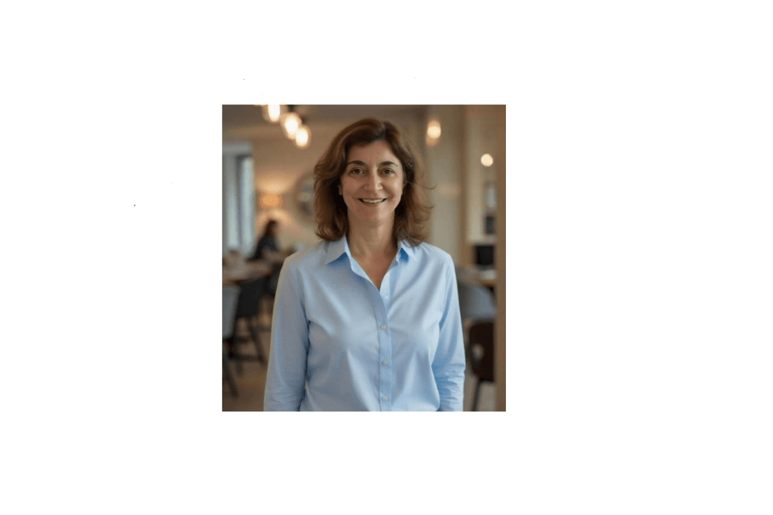 Smiling woman with brown hair wearing a light blue button-down shirt in an office.